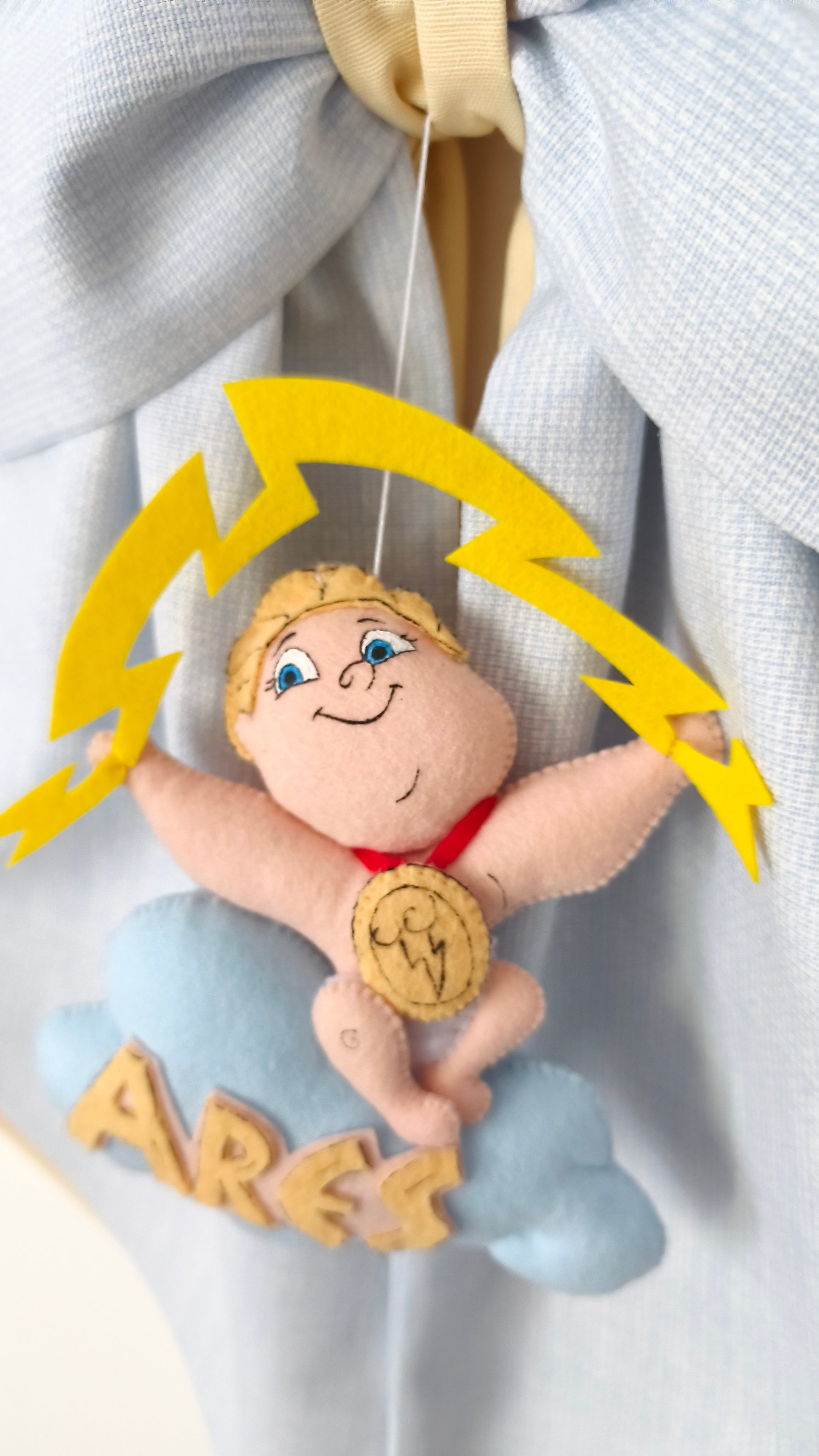 Dettaglio artigianale di Hercules in feltro su nuvola azzurra con fulmine giallo e nome Ares applicato a mano.