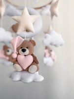 Dettaglio di orsetto in feltro marrone con cappellino rosa e cuore, cucito a mano su una nuvola bianca per giostrina culla.