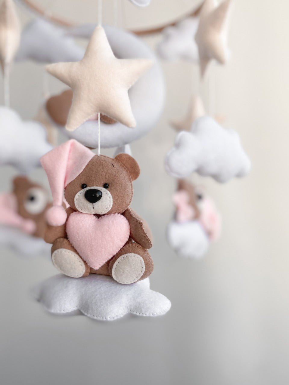 Dettaglio di orsetto in feltro marrone con cappellino rosa e cuore, cucito a mano su una nuvola bianca per giostrina culla.