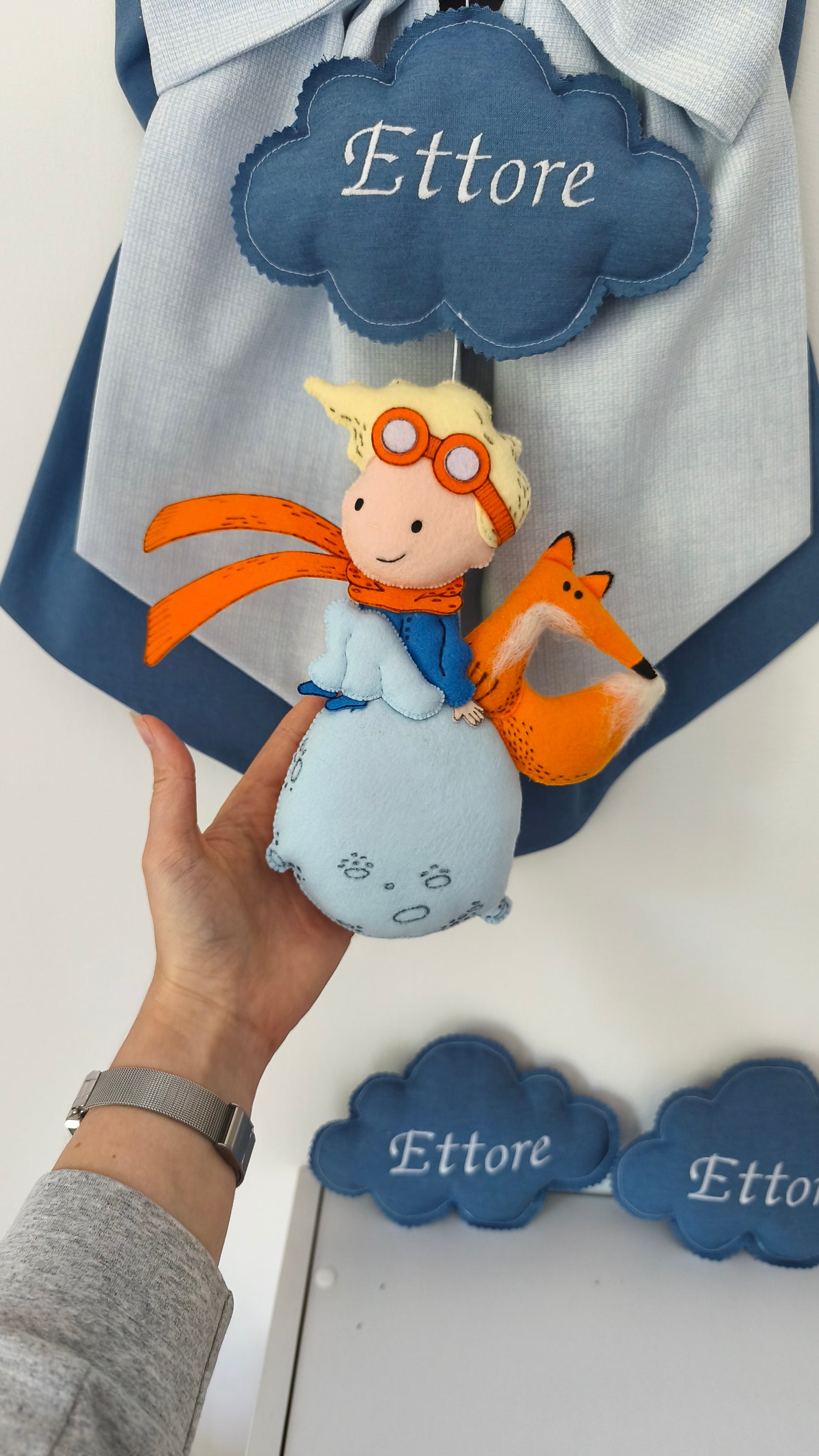Dettaglio Piccolo Principe e volpe in feltro cuciti a mano su pianeta azzurro, dimensioni reali mostrate in mano, fiocco nascita artigianale