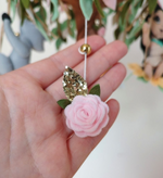 Dettaglio della rosa in feltro rosa e foglia glitter oro appesa alla giostrina musicale Pocahontas per neonati.