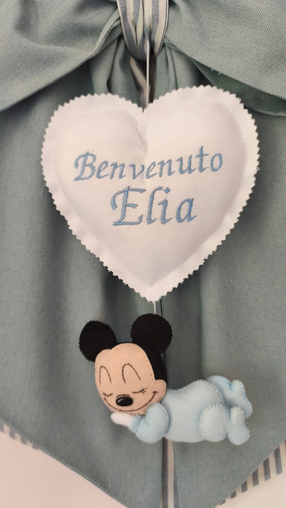Primo piano del personaggio Topolino neonato ricamato su fiocco nascita artigianale verde salvia