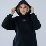 Donna sorridente indossa la felpa premaman nera Warm&Cosy tenendo il cappuccio, con ricamo bianco sul petto