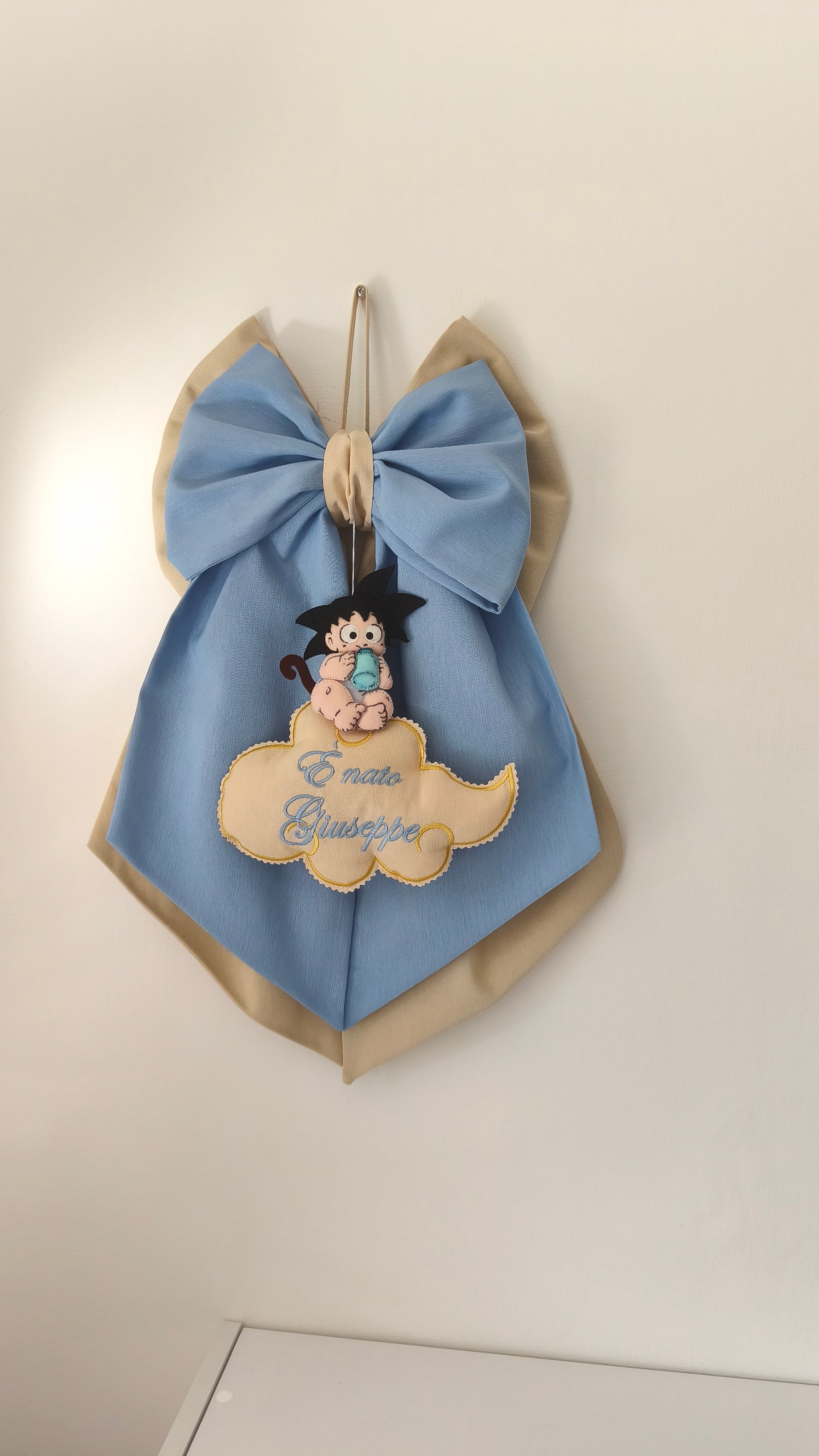 Fiocco nascita azzurro e beige personalizzato con Goku baby di Dragon Ball su una nuvoletta.