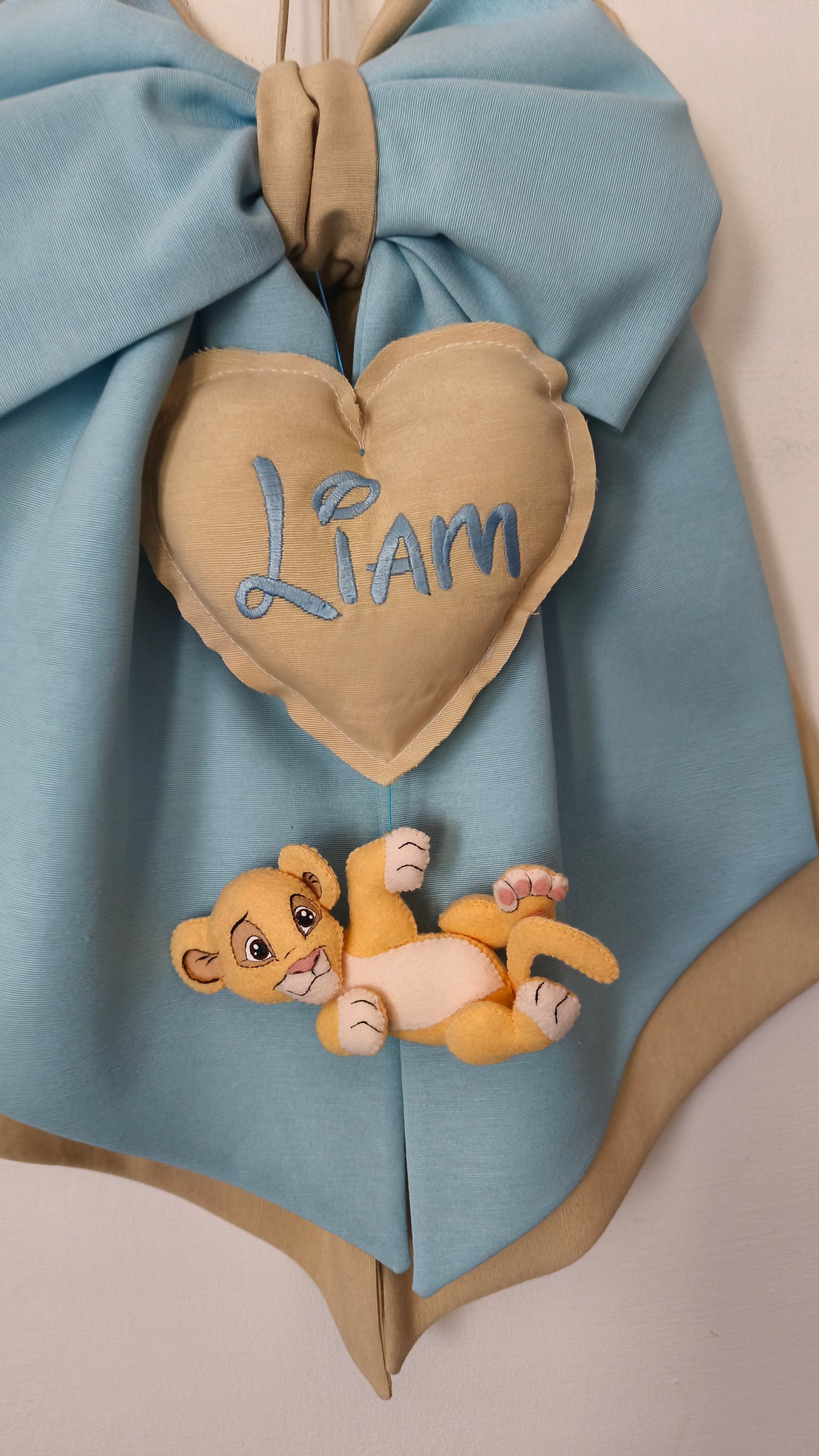 Fiocco nascita bimbo in tessuto azzurro e tortora con cuore beige, nome ricamato e leoncino decorativo – idea regalo nascita per porta e culla