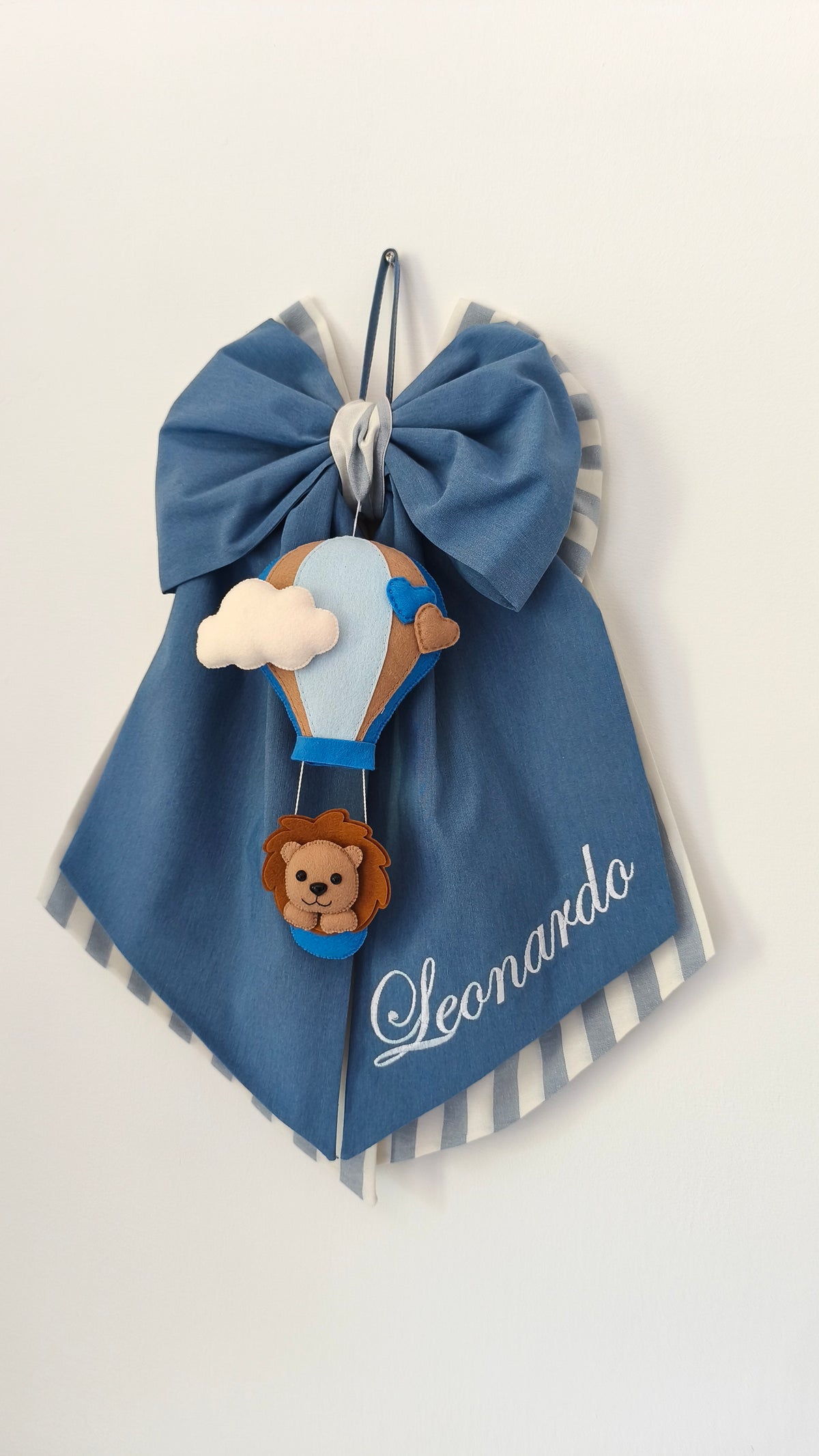 Fiocco nascita blu con mongolfiera in feltro, leoncino e nuvola, personalizzato con nome ricamato in corsivo.
