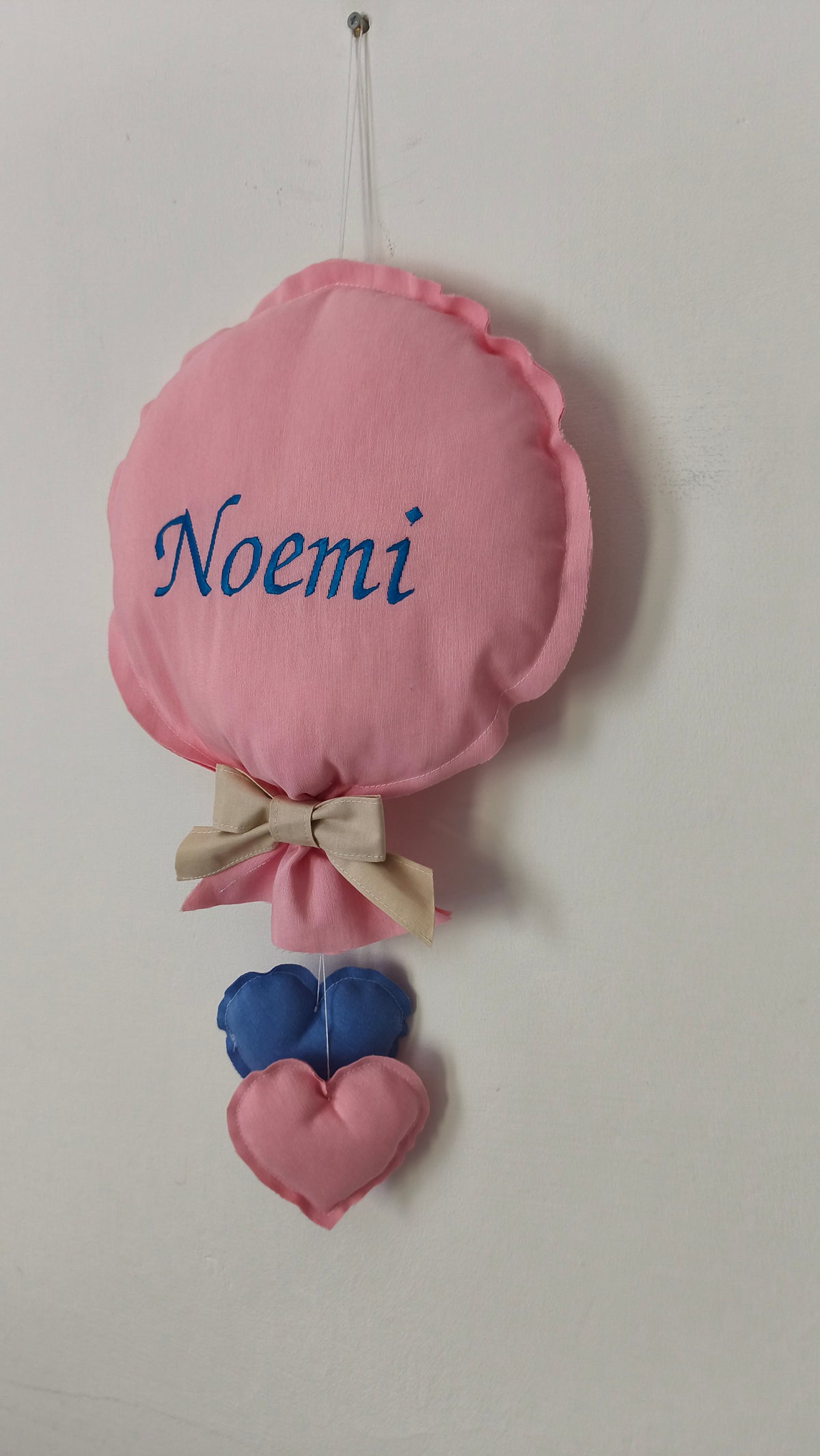 Fiocco nascita a forma di palloncino in cotone rosa con nome ricamato a mano in blu. Una decorazione artigianale imbottita con cuoricini pendenti, per porta della cameretta o alla culla in ospedale