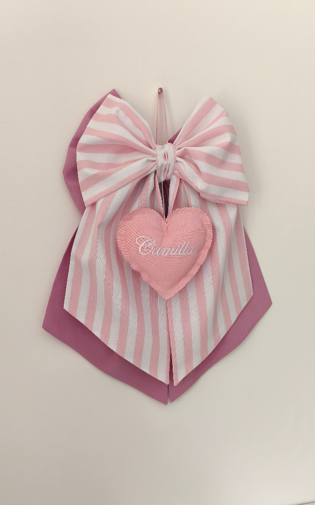 Fiocco nascita rosa e bianco a righe con cuore pendente centrale ricamato e doppio sfondo rosa scuro in tessuto.