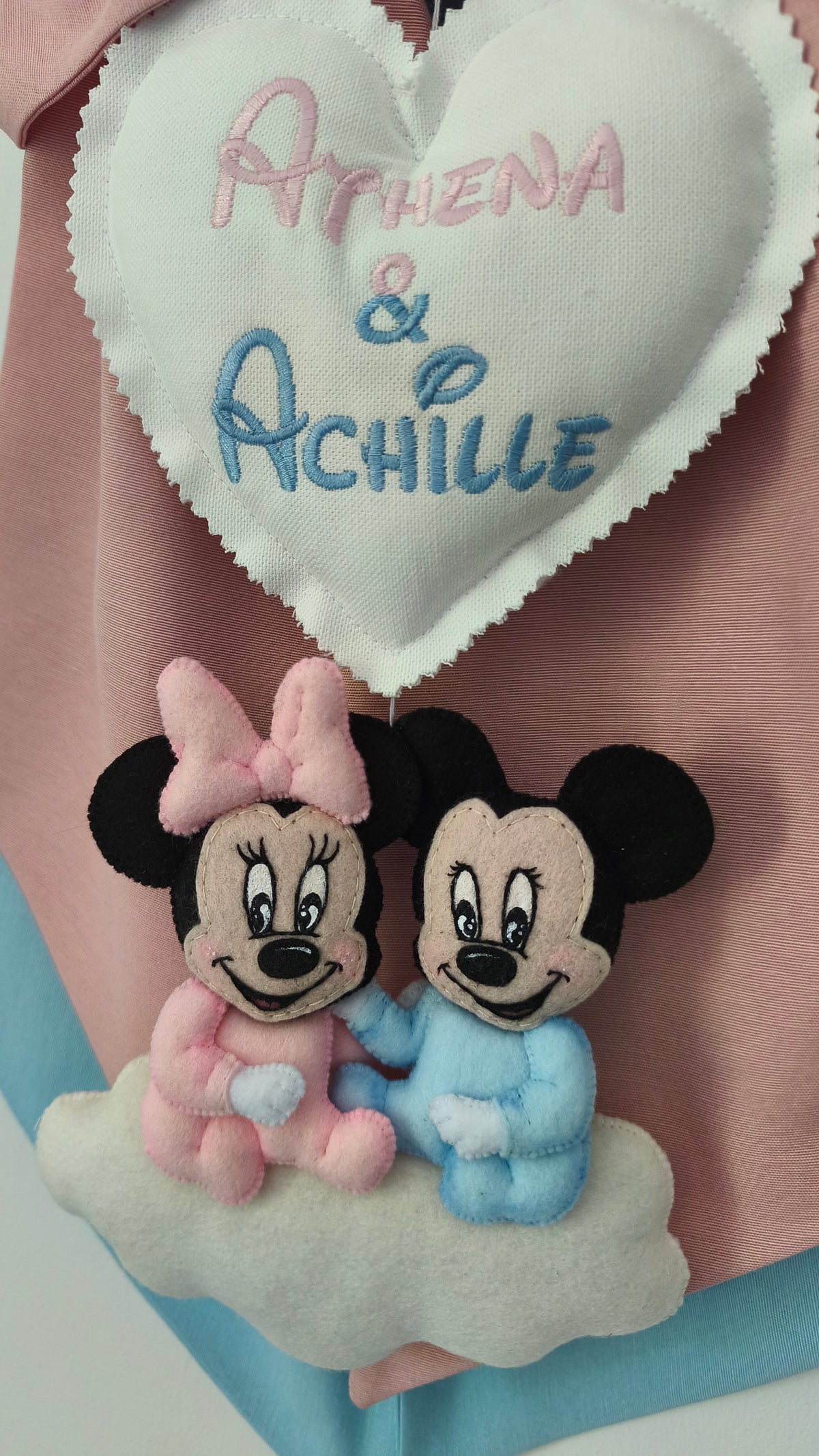 Primo piano cuore bianco ricamato con due nomi gemelli e coppia topolini Minnie e Mickey rosa azzurro in feltro cuciti a mano su nuvola