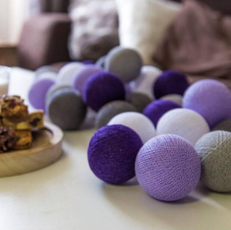 Palline di cotone luminose viola grigio e bianco su tavolo, ghirlanda decorativa