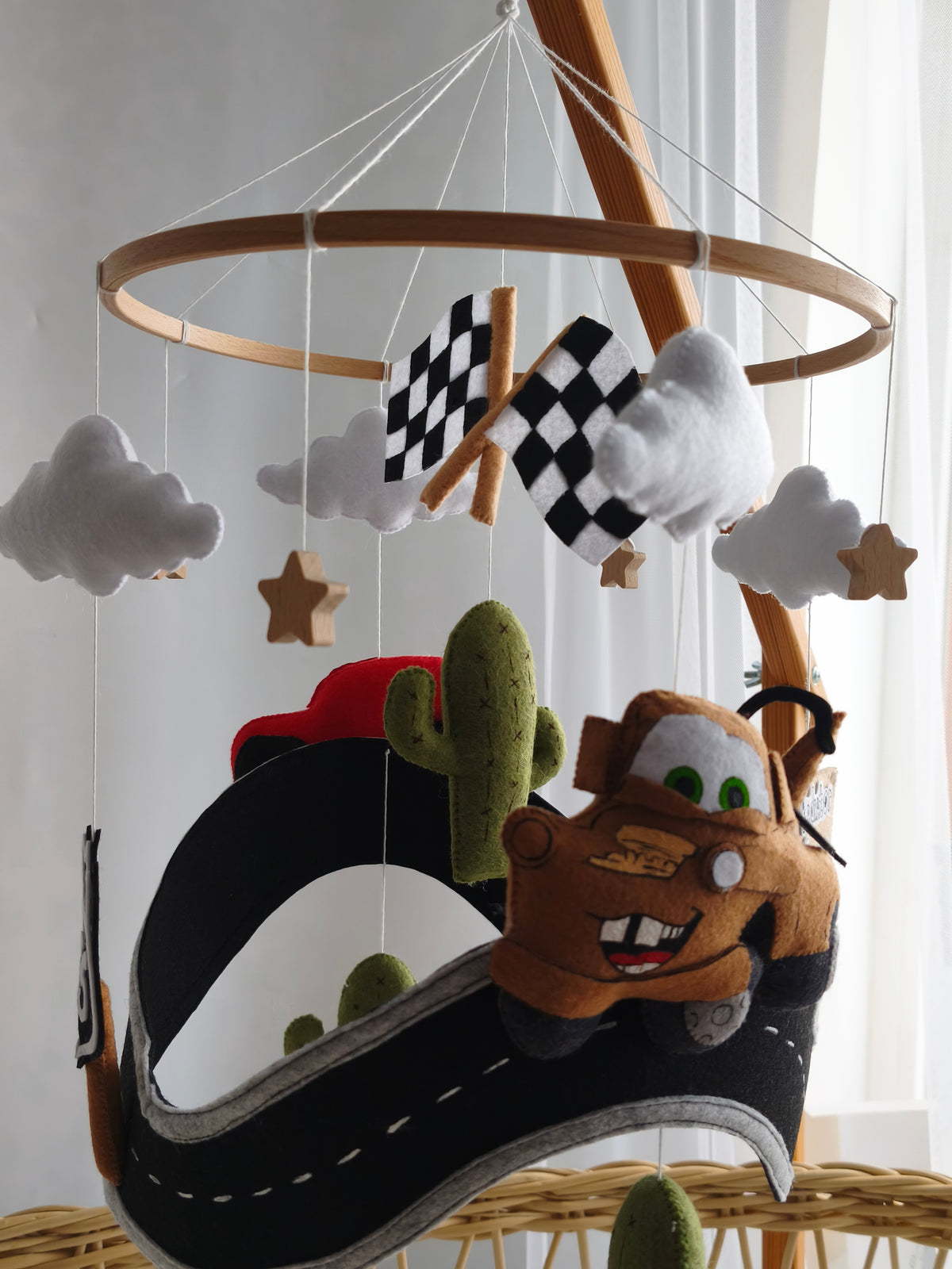 Giostrina feltro Cars con Cricchetto marrone su pista, cartello Radiator Springs, bandiere scacchi e cactus.