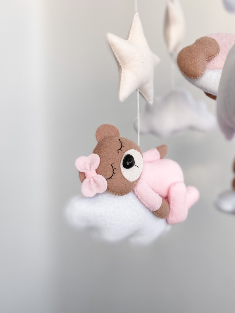 Primo piano di un orsetto in feltro rosa e marrone con fiocchetto, carillon neonata fatto a mano