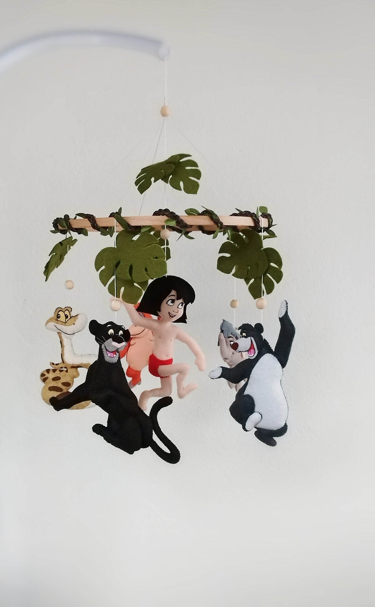 Giostrina Libro della Giungla in feltro con Mowgli, Bagheera nera, Baloo grigio e foglie verdi tropicali.