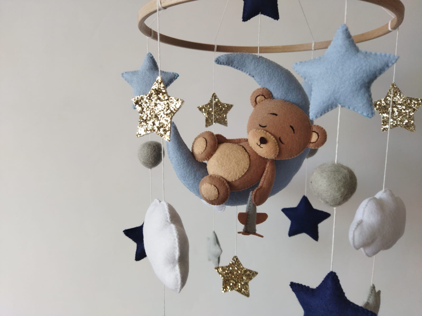 Dettaglio giostrina musicale culla orsetto addormentato luna azzurra stelle oro glitter blu navy nuvole bianche feltro neonato