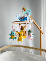 Giostrina neonato Pokémon fatta a mano con Pikachu, Squirtle, Jigglypuff e Primarina appesi sopra la culla.