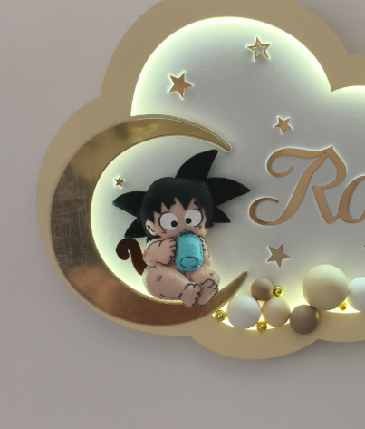 Dettaglio Goku baby in feltro con biberon azzurro seduto sulla luna oro, luce notturna a nuvola con LED e stelle