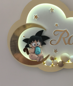 Dettaglio Goku baby in feltro con biberon azzurro seduto sulla luna oro, luce notturna a nuvola con LED e stelle
