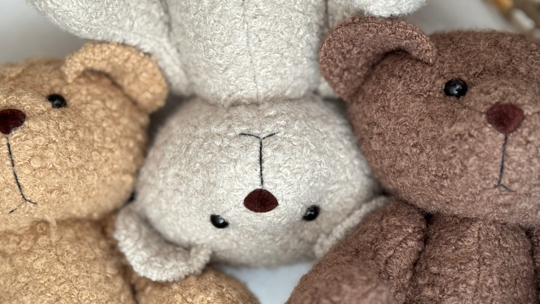 Tre orsetti di peluche in tessuto riccio nei colori beige, panna e marrone scuro per neonati