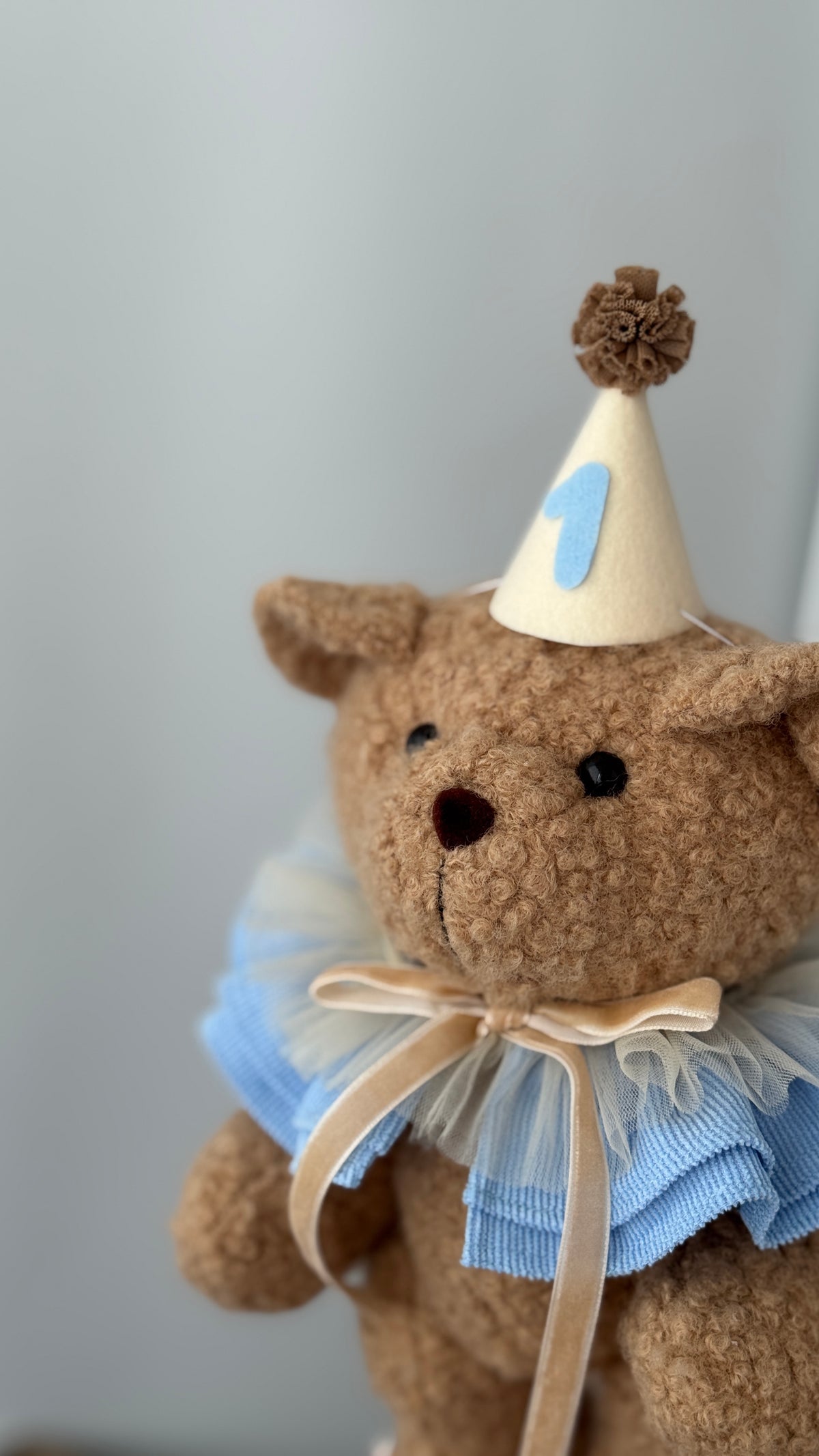 Orsetto di peluche beige con colletto a balze azzurro e cappellino col numero 1 per neonati