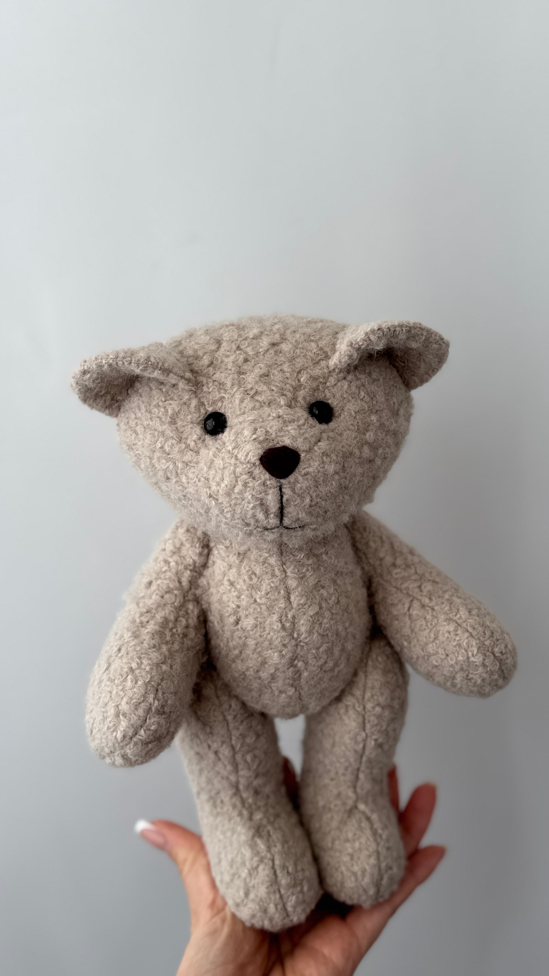 Orsetto di peluche color panna in morbido tessuto riccio per bambini sorretto da una mano