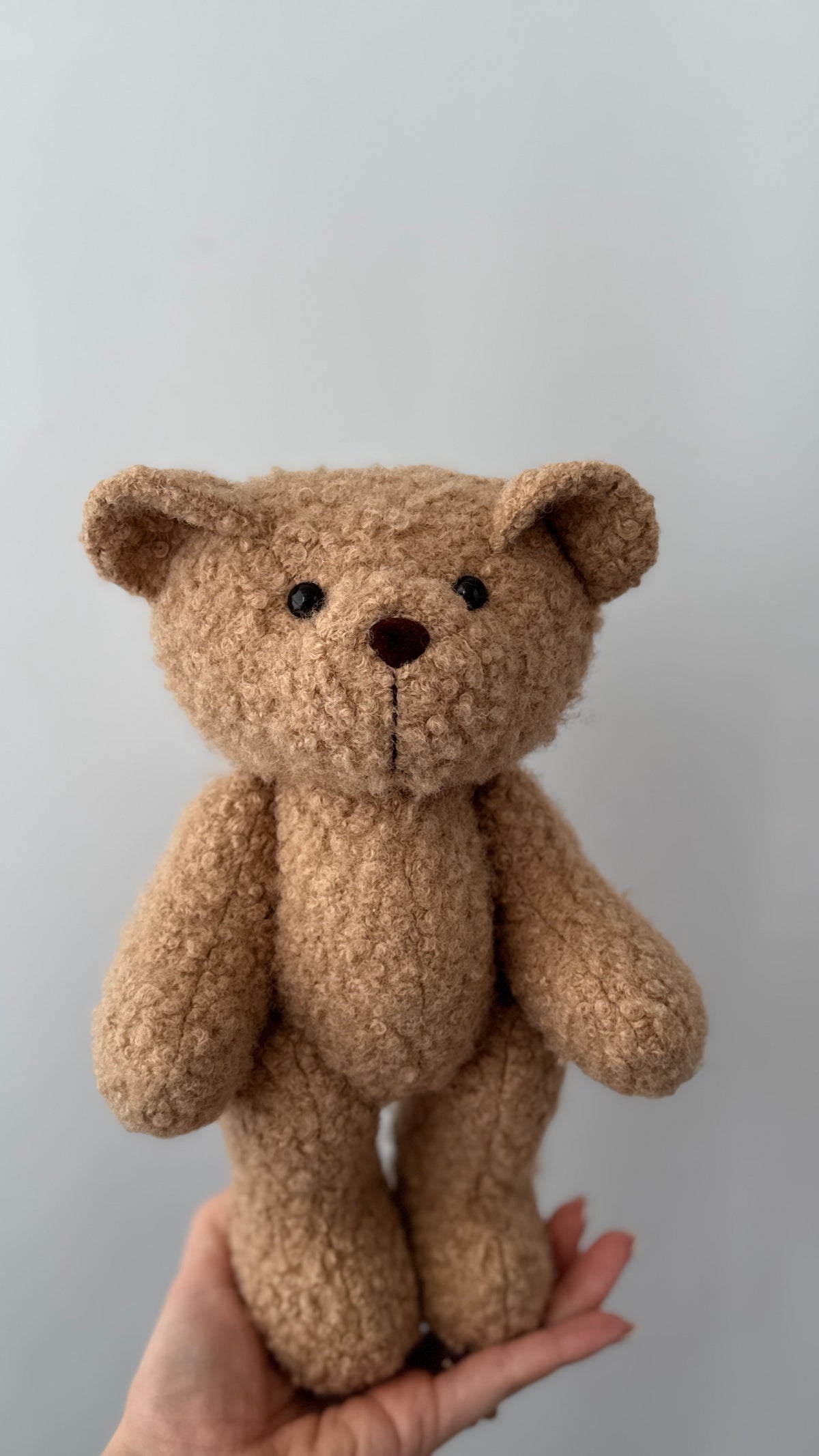 Orsetto di peluche beige in morbido tessuto bouclè riccio per bambini sorretto da una mano