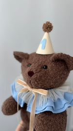 Primo piano di un orsetto marrone di peluche con colletto azzurro e cappellino col numero 1