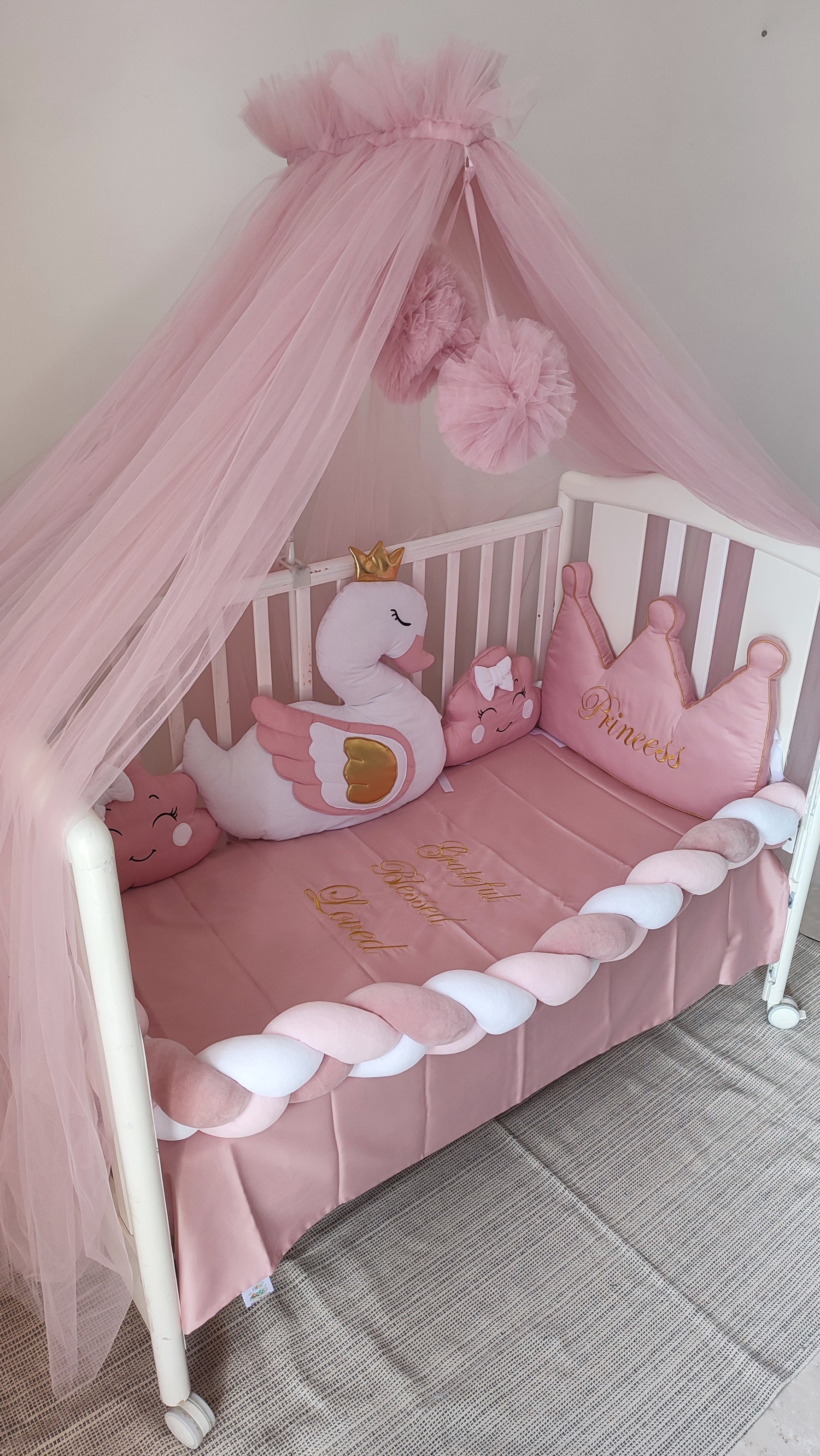 Culla neonato con paracolpi intrecciato rosa e cuscini sagomati personalizzabili con ricami dorati per cameretta.