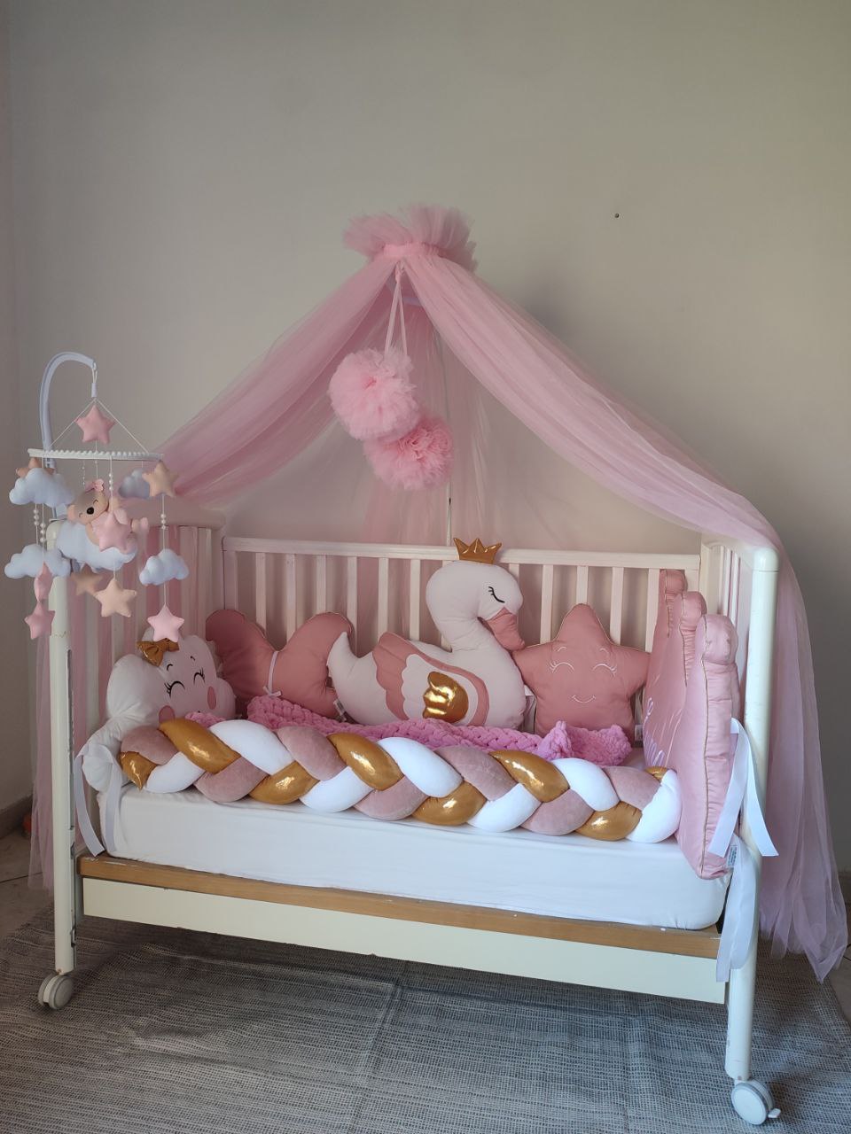 Culla neonato con paracolpi intrecciato rosa, morbida coperta ciniglia e cuscini sagomati a corona per cameretta.