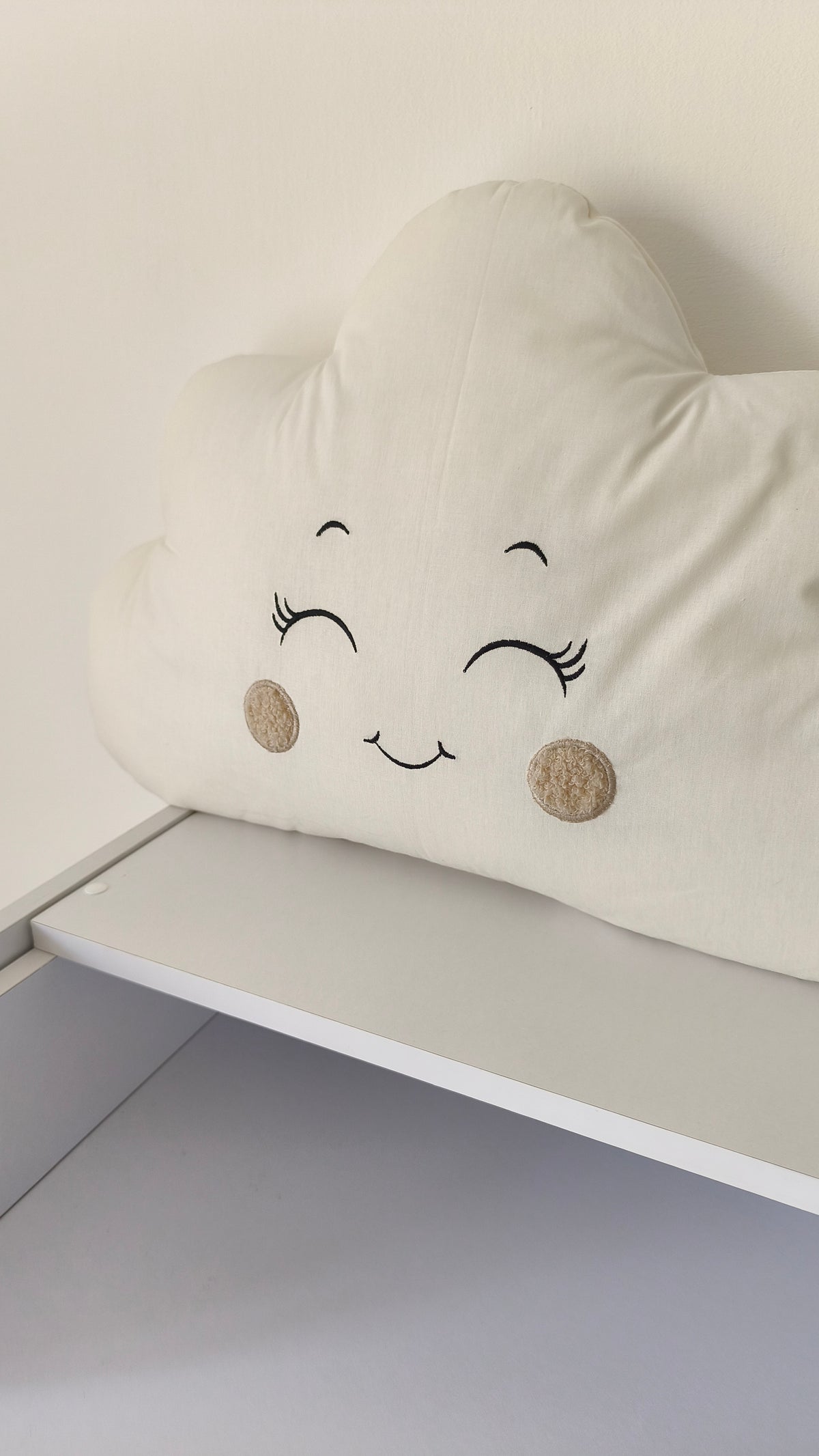 Cuscino decorativo a nuvola in tonalità calde e neutre, appoggiato su un mobile bianco per la cameretta dei neonati.