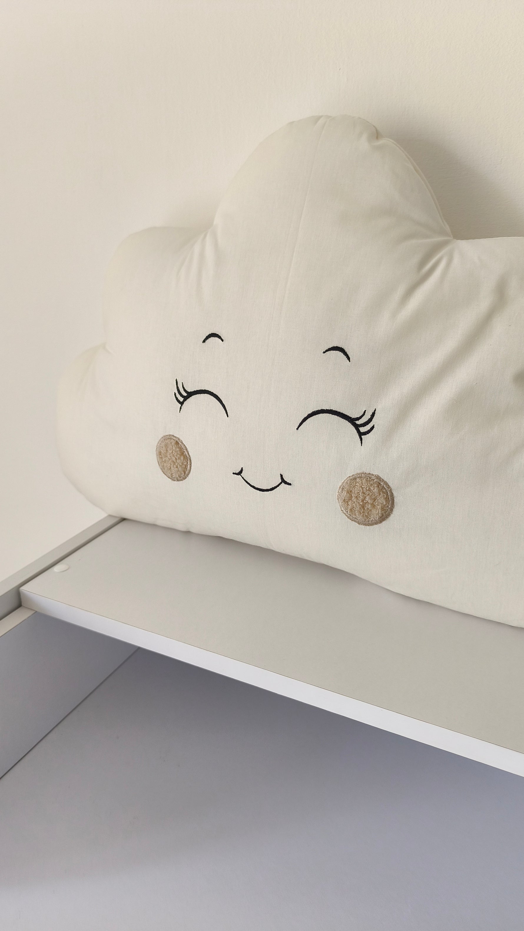 Cuscino decorativo a nuvola in tonalità calde e neutre, appoggiato su un mobile bianco per la cameretta dei neonati.