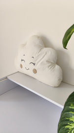 Primo piano di un cuscino paracolpi a forma di nuvola panna con occhi ricamati e guance beige per lettino neonato.