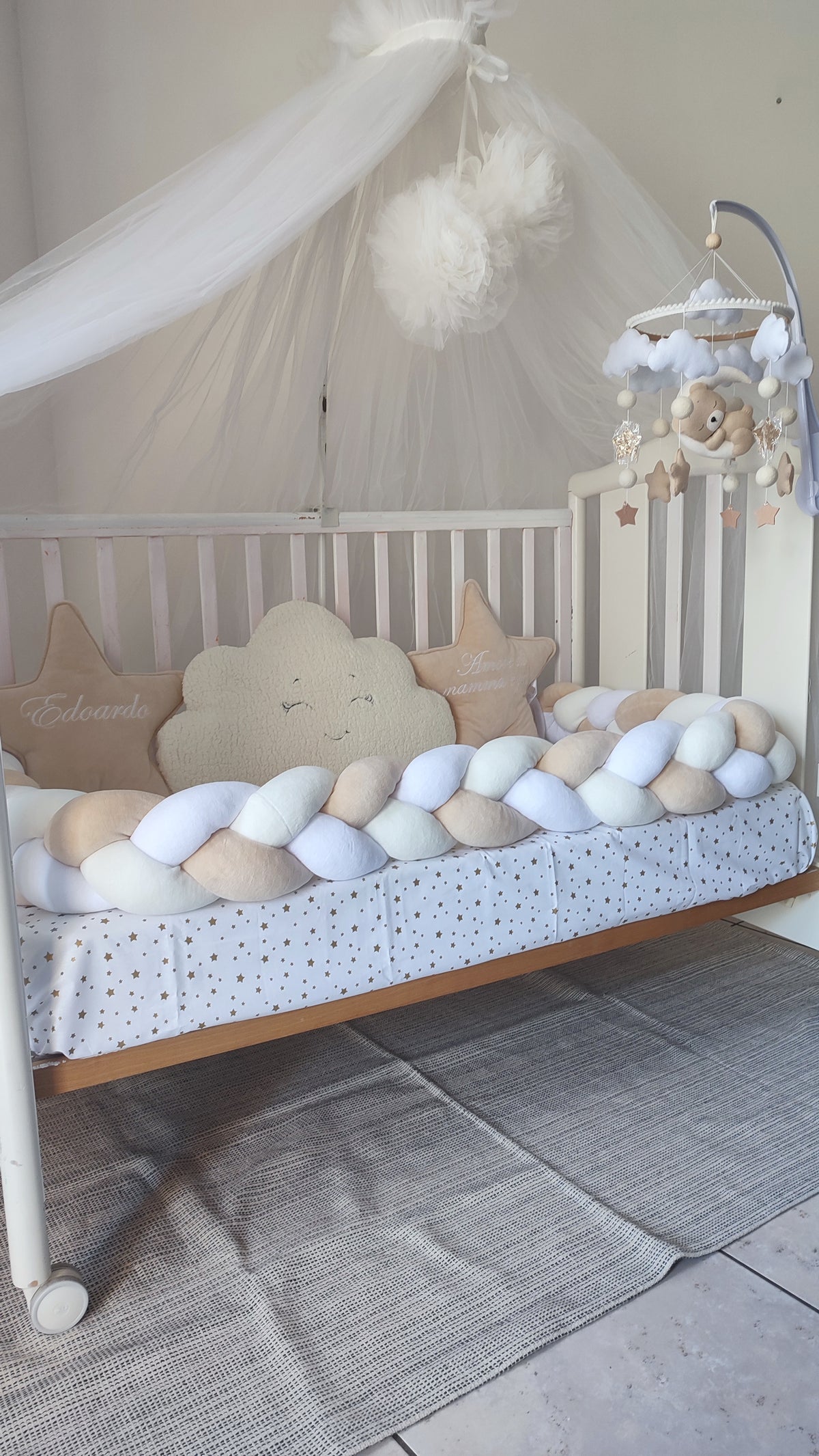 Primo piano di un paracolpi a treccia bianco e beige per lettino con cuscini a stella personalizzati e cuscino nuvola morbido.