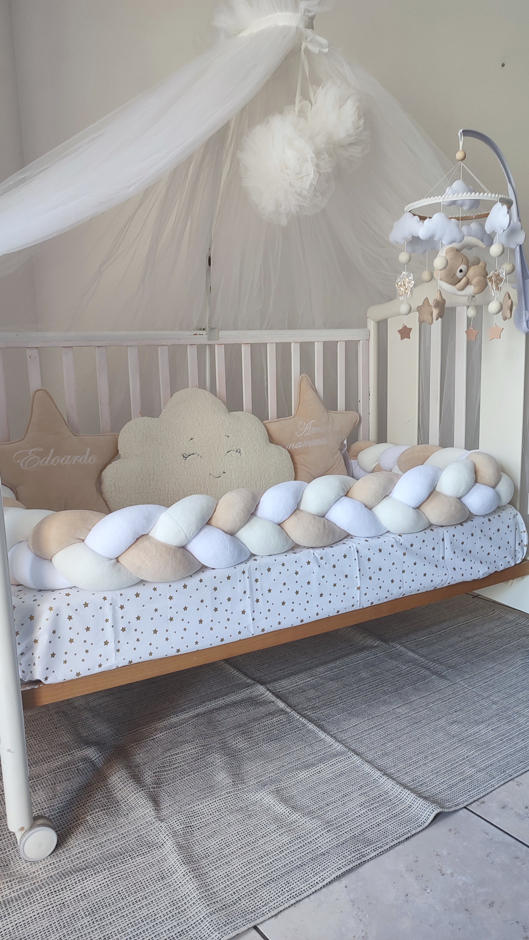 Primo piano di un paracolpi a treccia bianco e beige per lettino con cuscini a stella personalizzati e cuscino nuvola morbido.