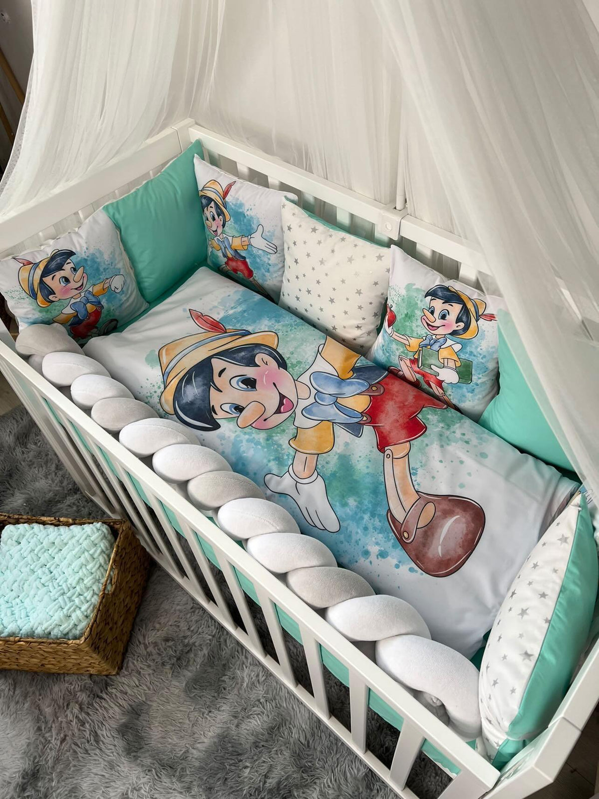Set lettino neonato con paracolpi a treccia bianco e cuscini sfoderabili a tema Pinocchio in una culla bianca con velo