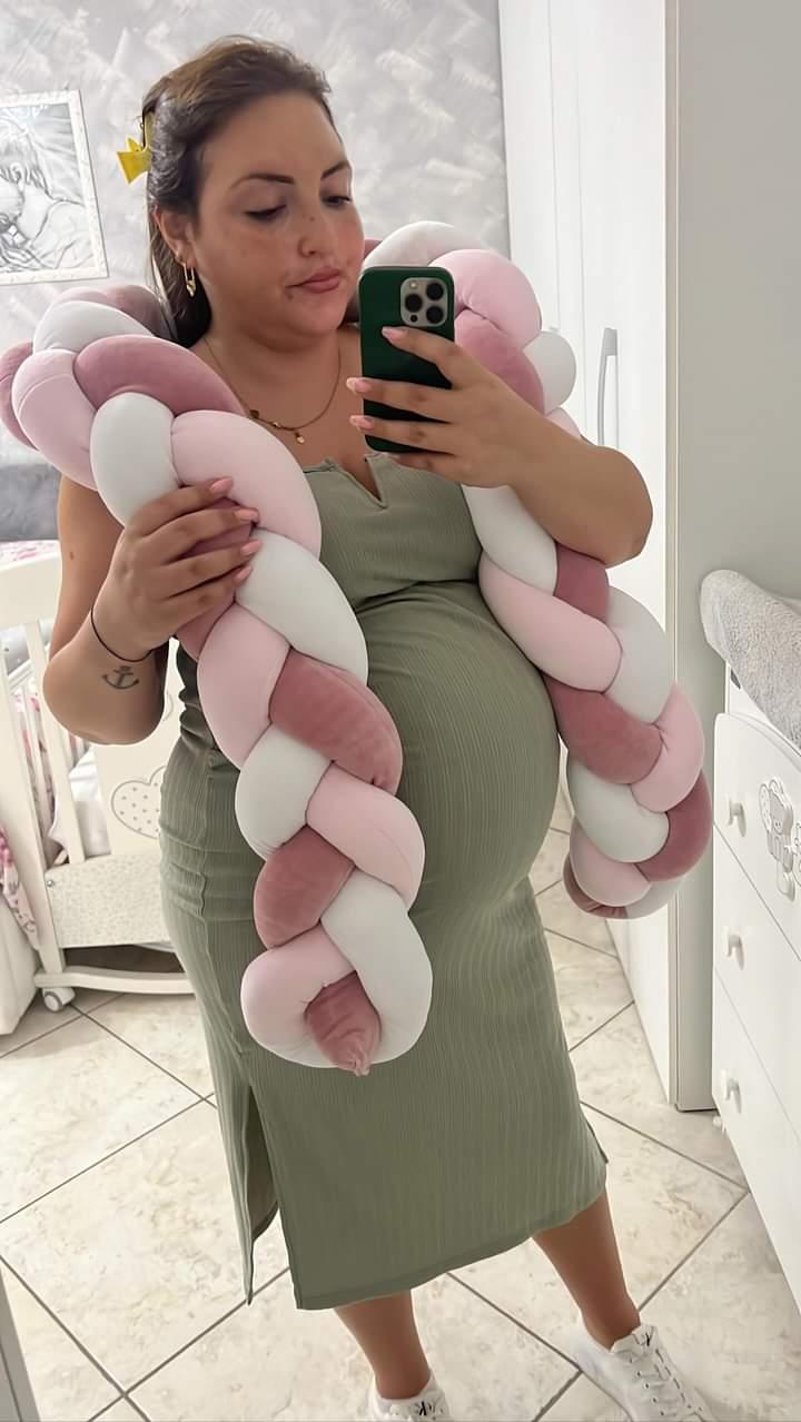 Mamma in dolce attesa con paracolpi intrecciato a tre colori per neonati, ideale per l'allestimento della culla.