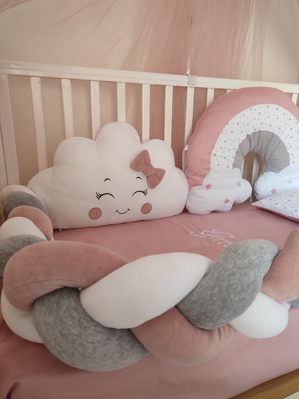 Set lettino con paracolpi a treccia bianco, grigio e rosa, cuscino a nuvoletta con fiocco e morbido arcobaleno a stelline.