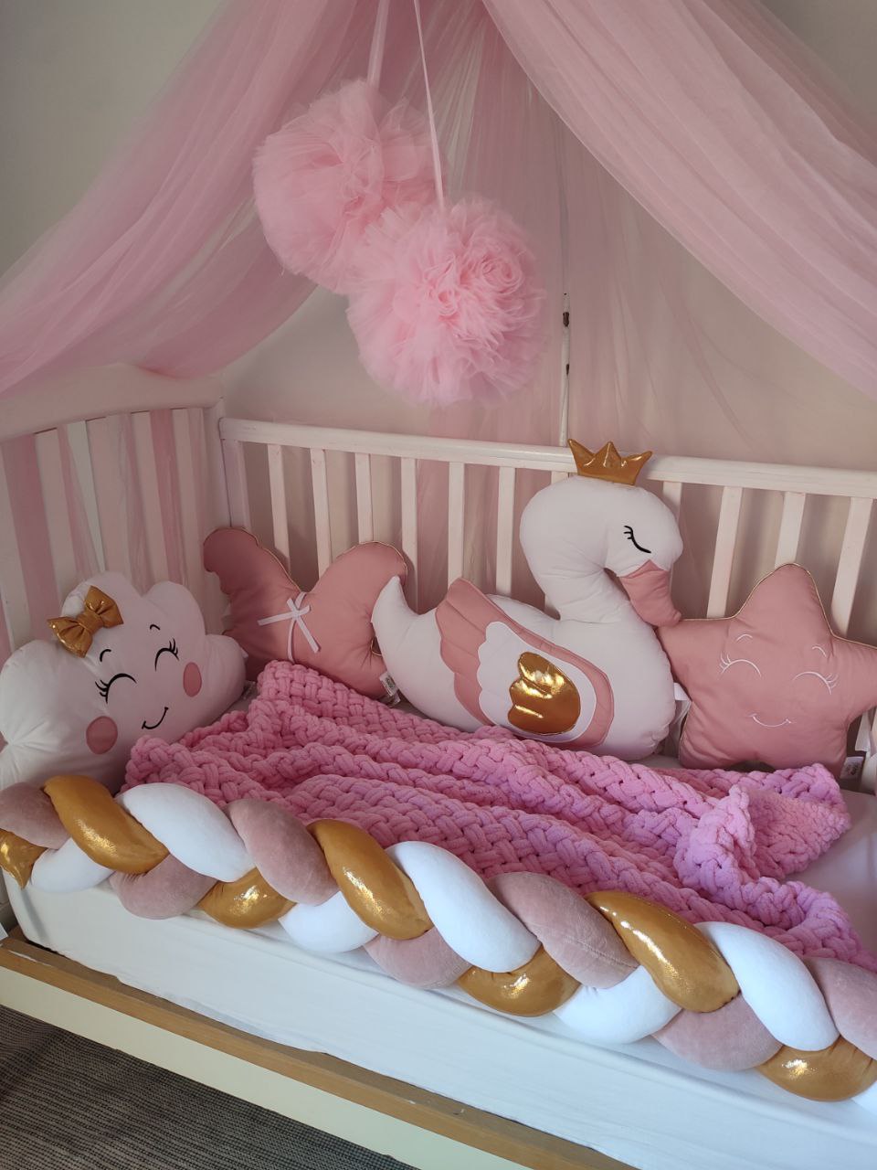Lettino neonato con paracolpi intrecciato bianco e rosa, coperta a maglia e cuscini decorativi per cameretta bimba.