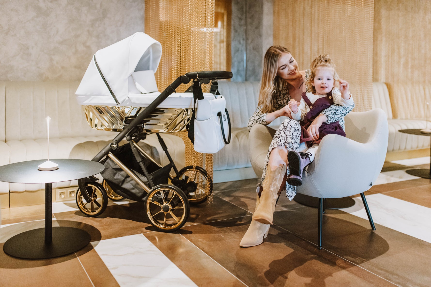 Kunert Ivento Glam navicella bianco perla telaio dorato e ruote oro, mamma con bimba in ambiente elegante, lifestyle interior