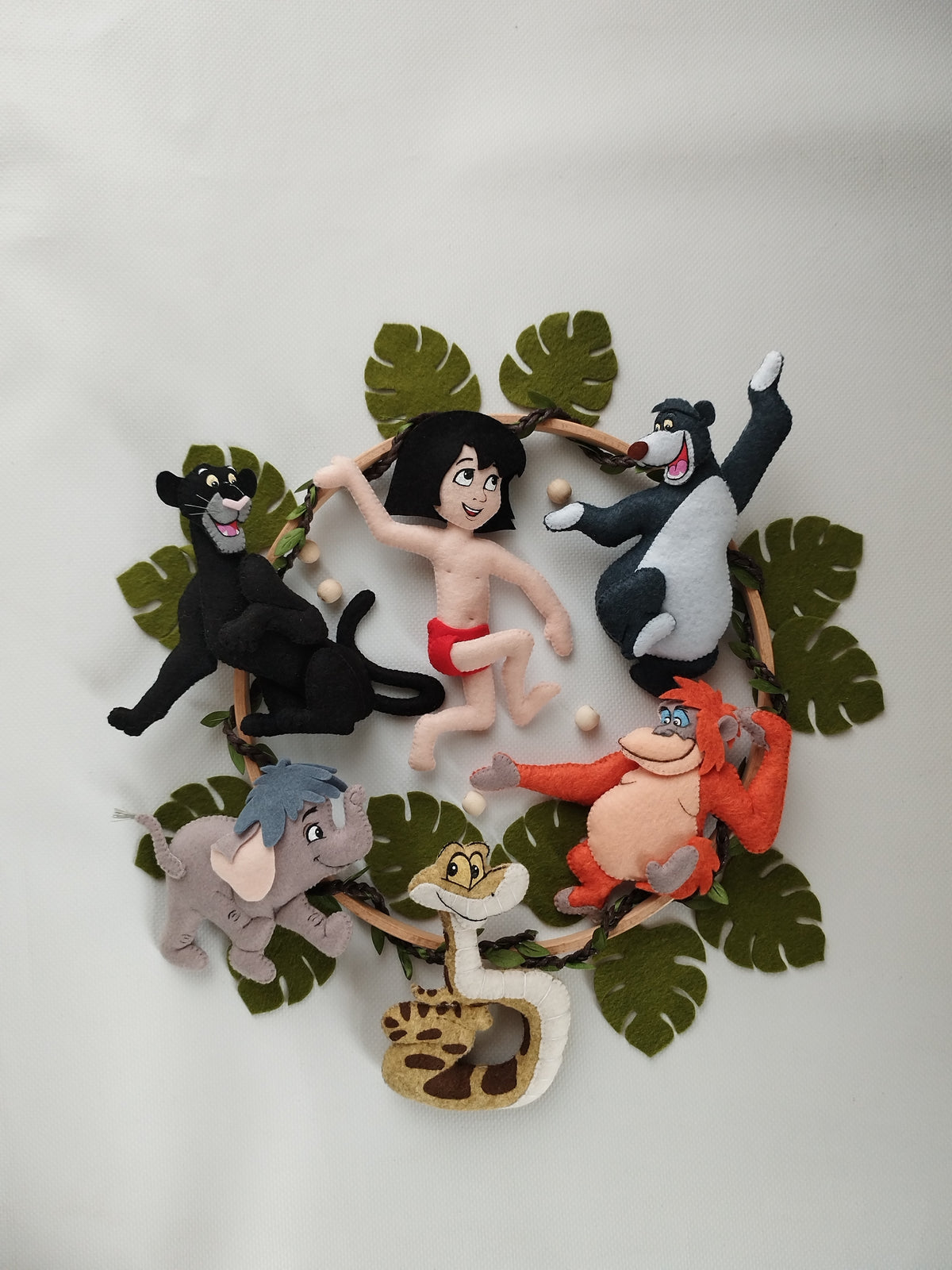 Personaggi feltro Libro della Giungla con Mowgli, Bagheera, Baloo, Re Luigi arancione e foglie su sfondo bianco.