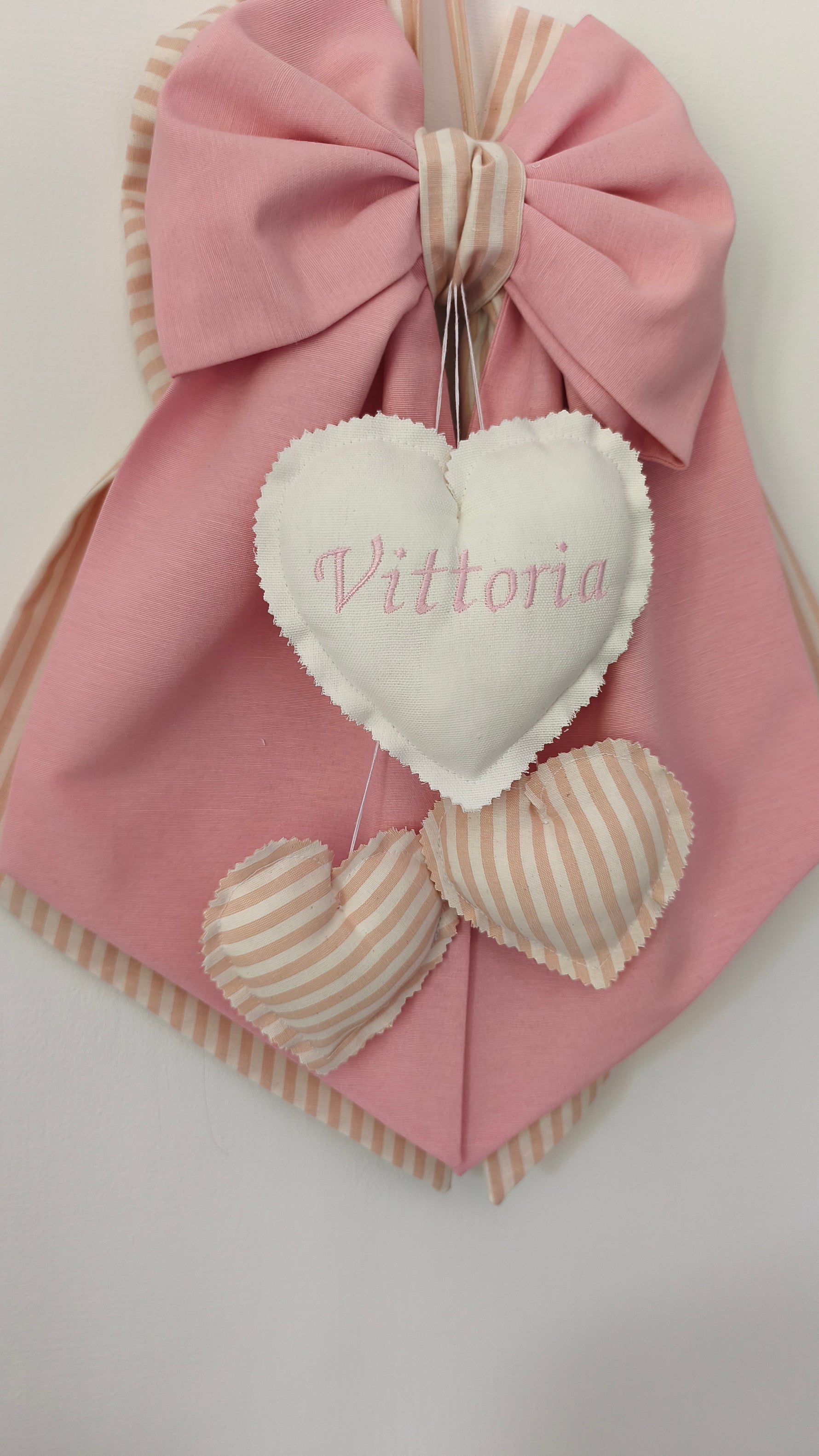 Primo piano cuoricino con nome bimba ricamato, fiocco rosa e cuori beige a righe