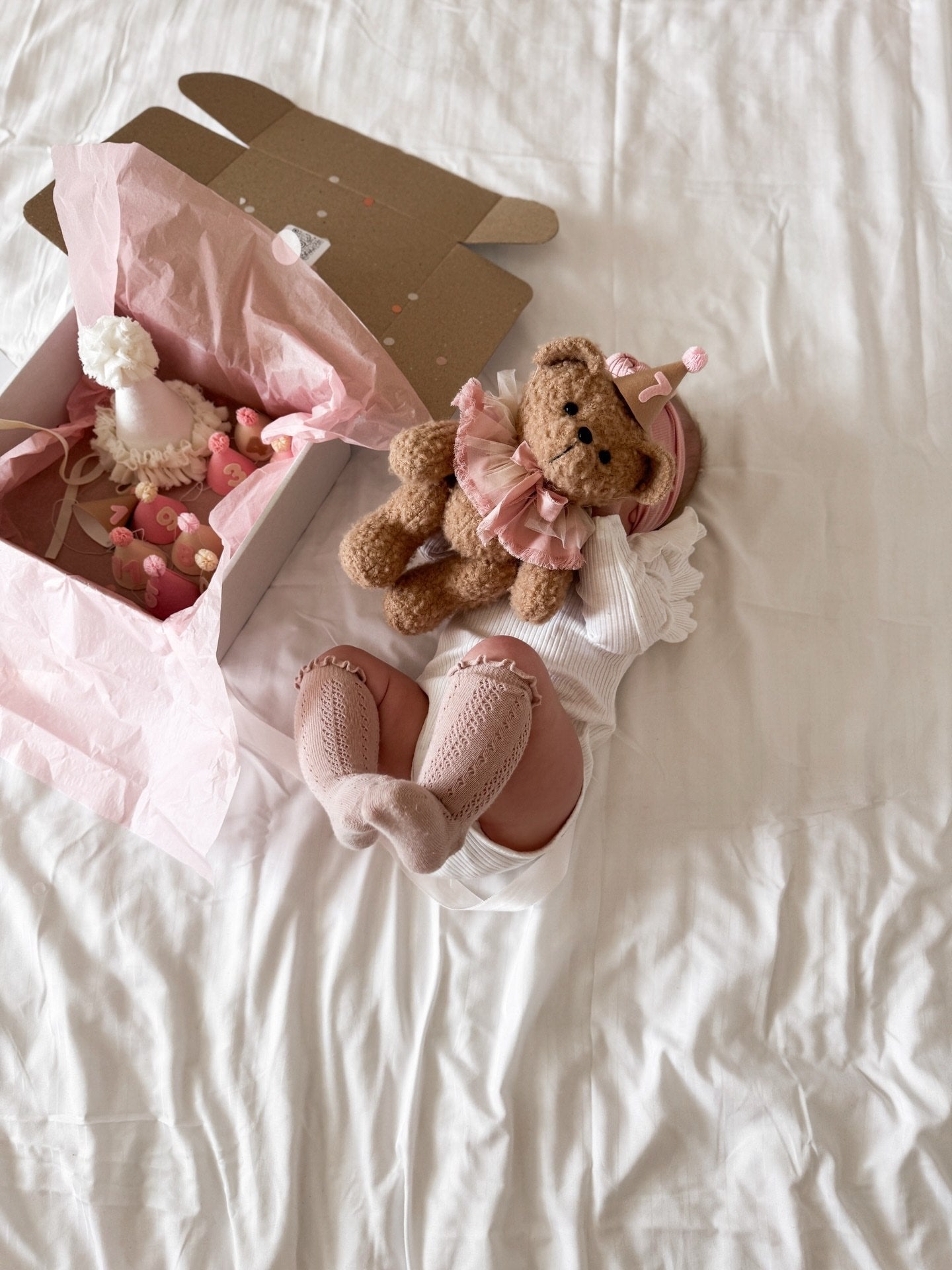 Neonata sul letto con un orsetto di peluche e scatola regalo con cappellini per i mesi