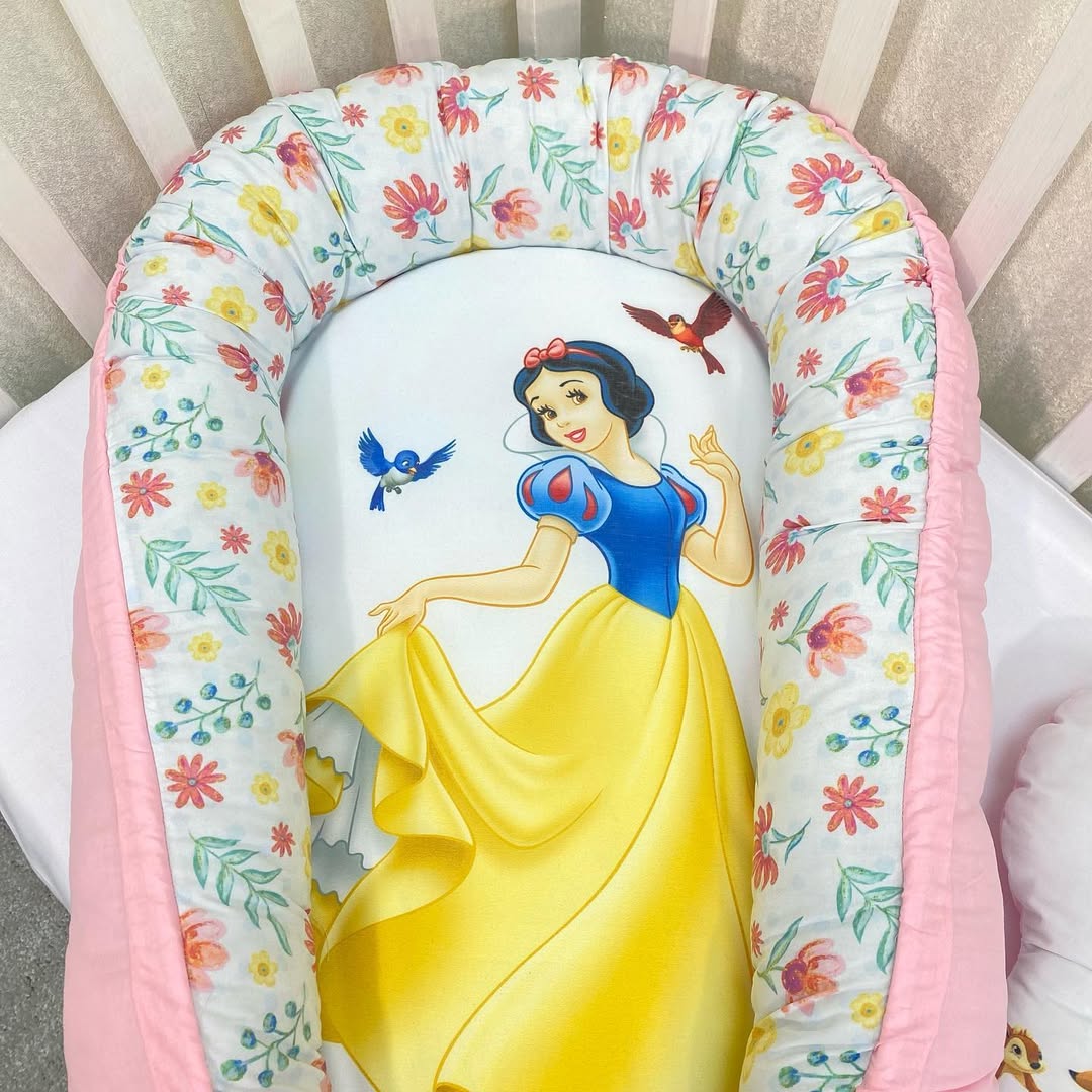 Riduttore nido Biancaneve con vestito giallo e bordi a fiori rossi e verdi, baby nest rosa confetto per culla neonata.
