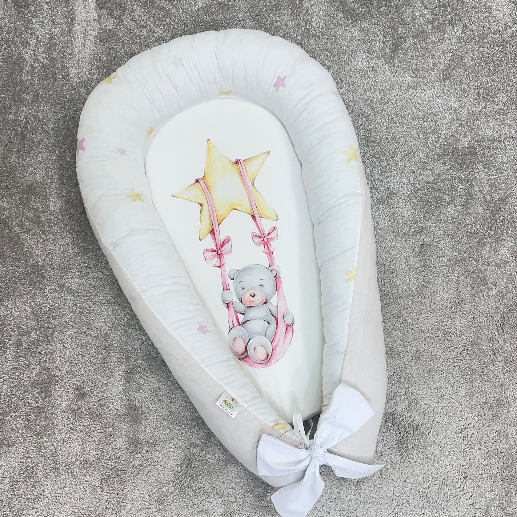 Riduttore nido per neonato beige con orsetto su altalena, fiocco bianco e bordi morbidi, ideale per lettino o culla