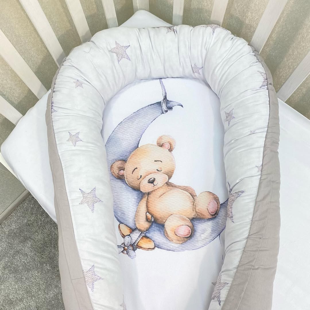 Riduttore nido neonato grigio con stampa orsetto sulla luna e stelline, posizionato nella culla