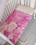 Sacco a pelo per bambini personalizzato con nome Ines, rosa con bambola bionda, steso in un lettino con cuscino beige