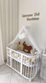 Allestimento culla neonato neutro con paracolpi intrecciato panna e marrone, cuscini peluche bouclé e velo con pon pon.