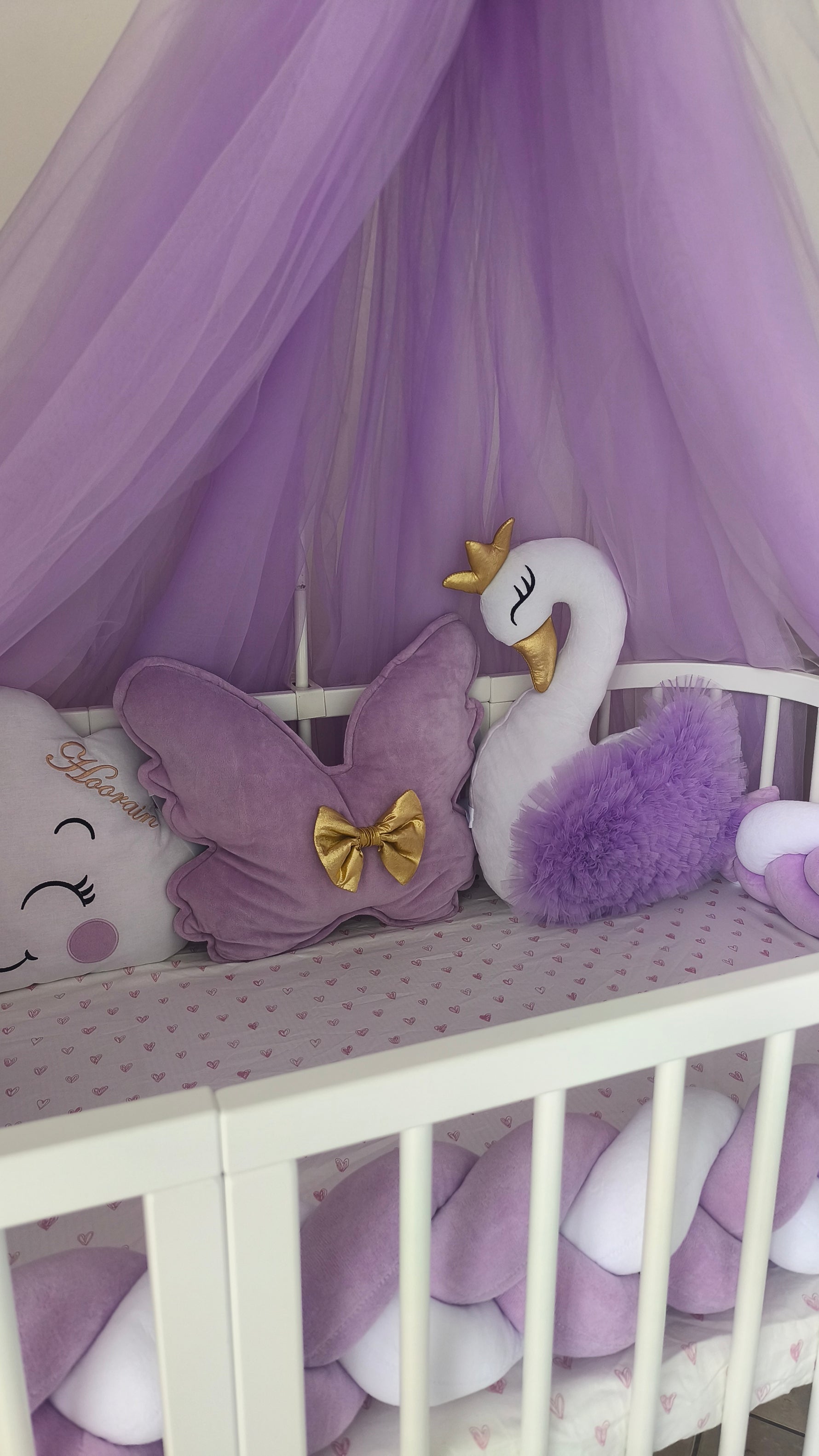 Dettaglio cuscino a nuvola con nome e fiocco viola, inserito in un set culla completo lilla e bianco con cigno.
