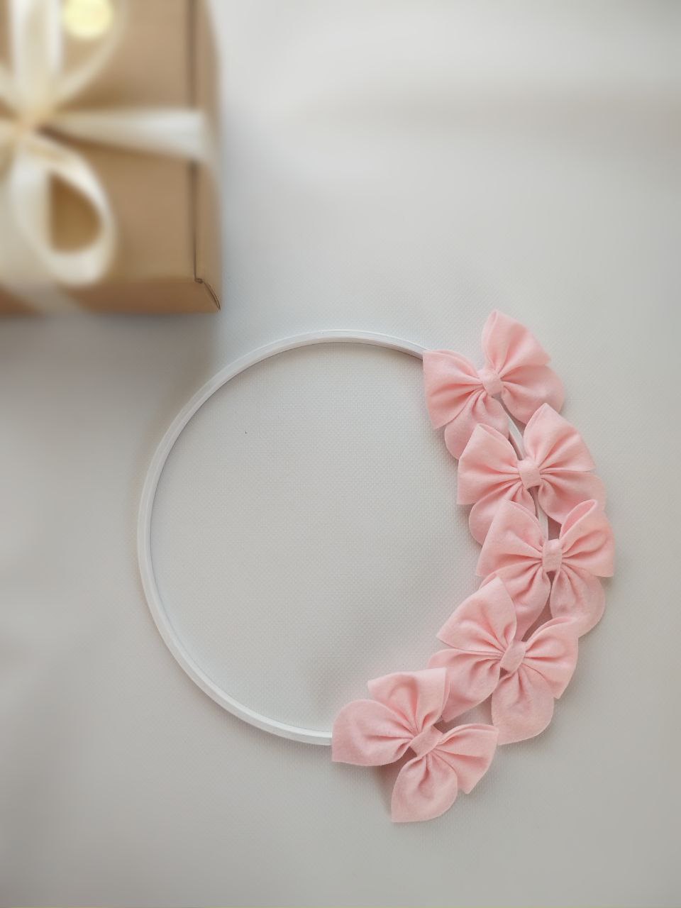 Dettaglio struttura per giostrina neonato con cerchio bianco decorato da grandi fiocchi rosa in feltro.
