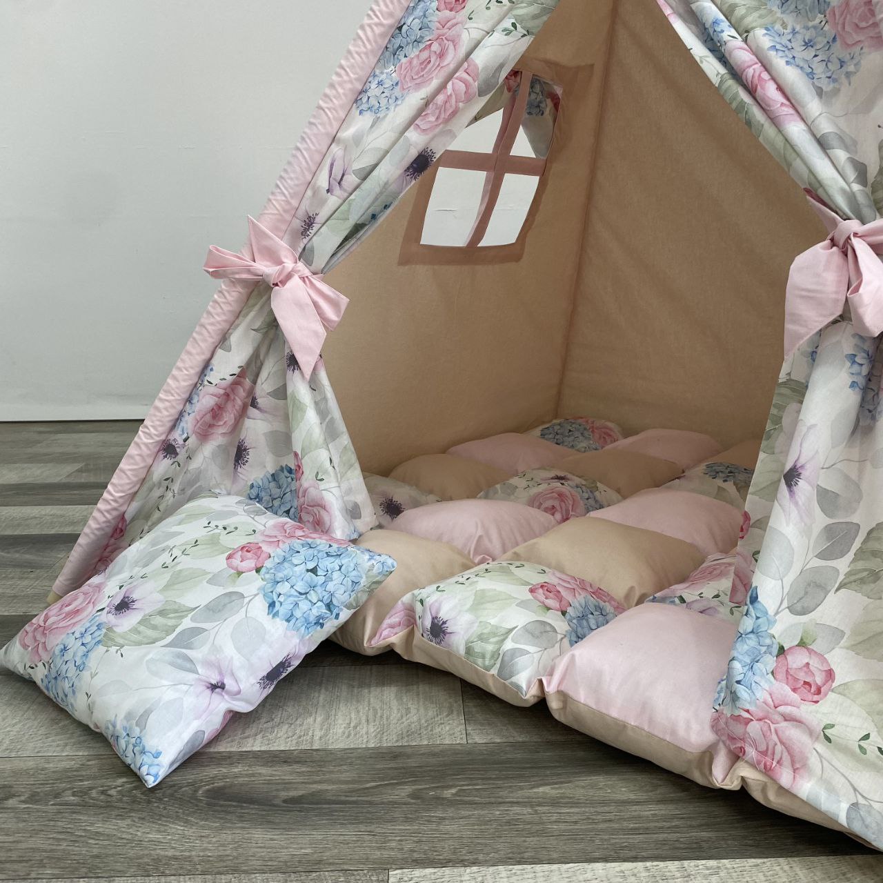 Interno teepee bambina beige con tappeto a scacchi rosa, cuscini floreali e fiocchi rosa