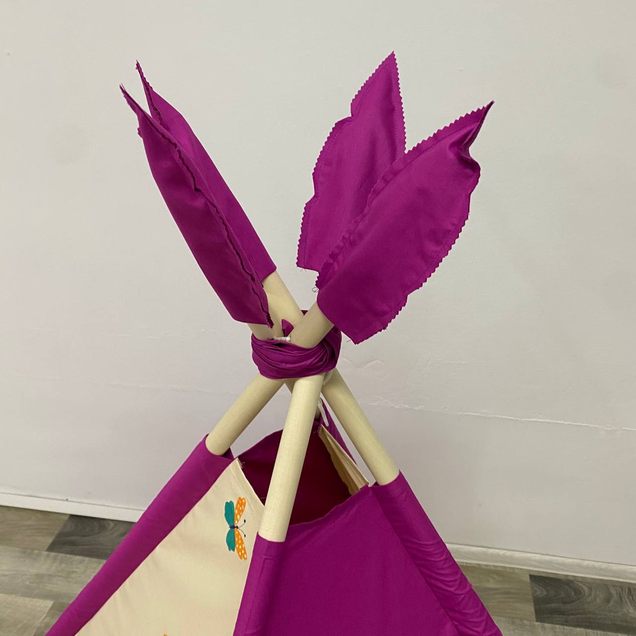 Dettaglio cima tenda teepee bambini con pali in legno di tiglio e piume fucsia decorativi